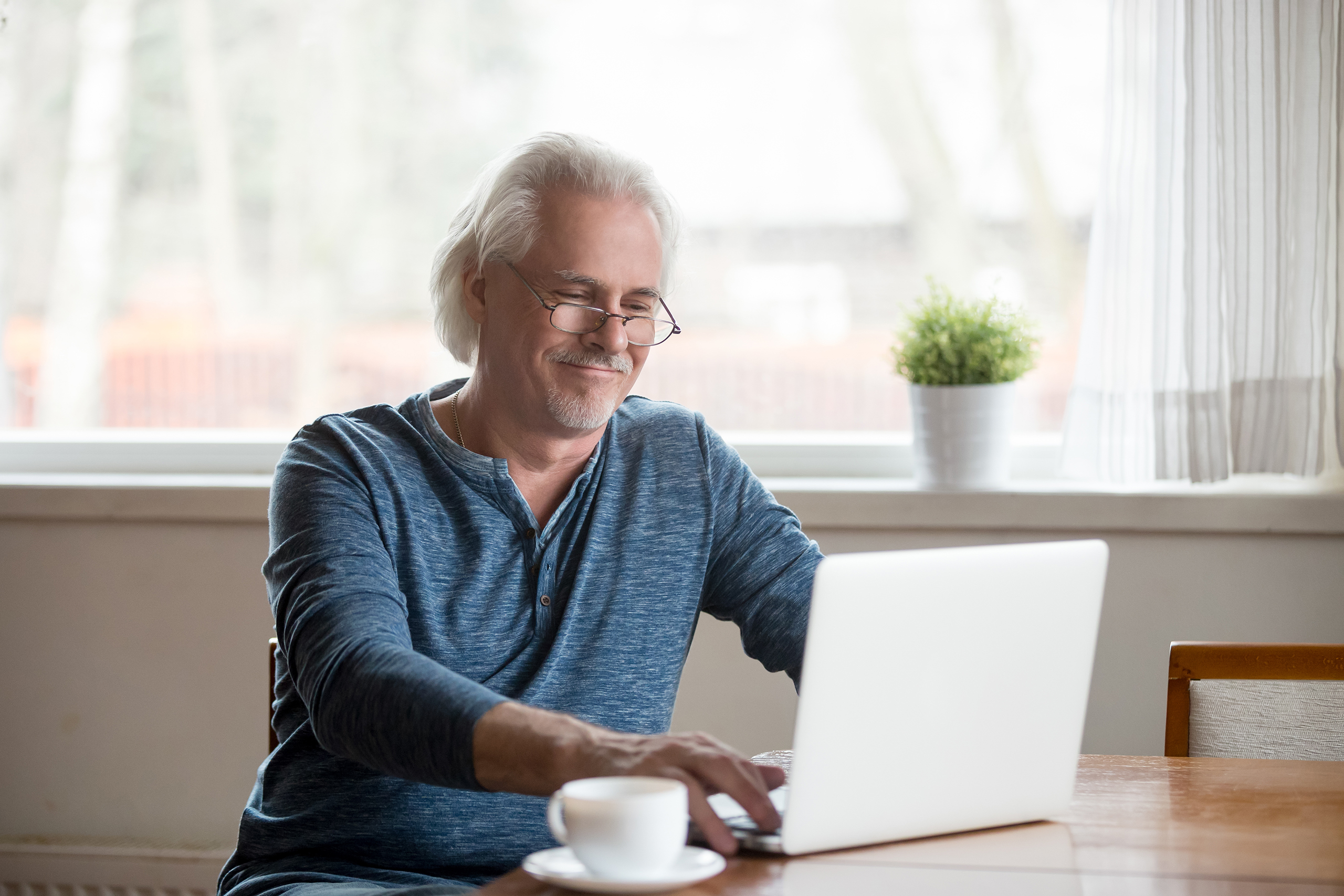 Smiling senior man in glasses working on laptop at home