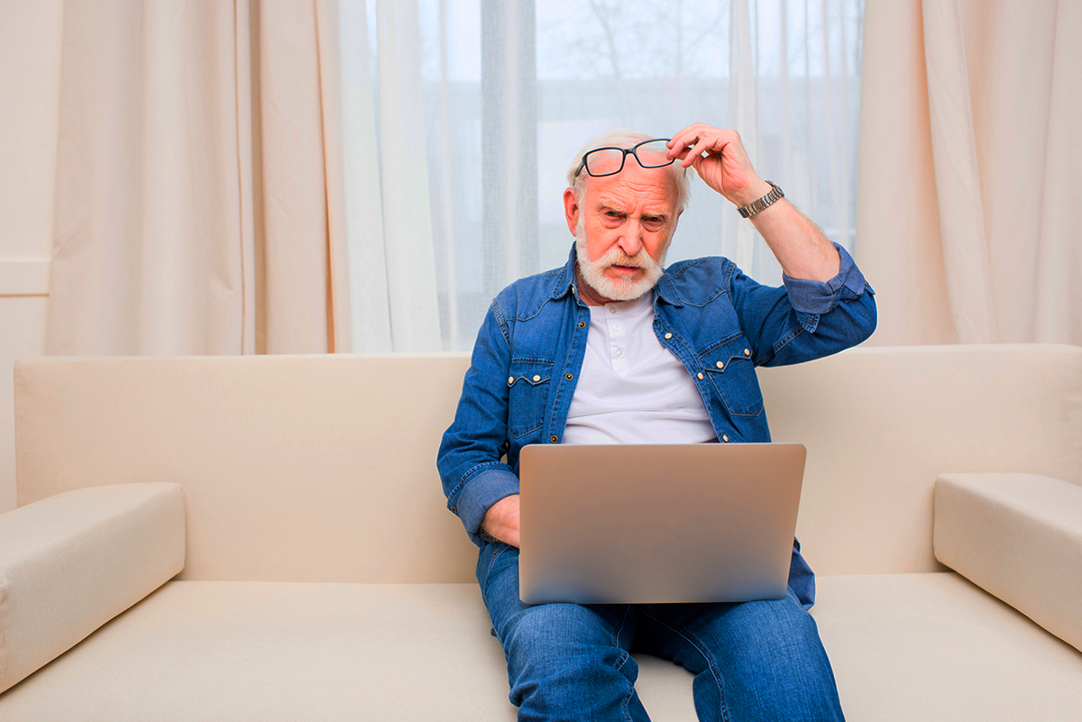 senior man sitting on couch looking confused at laptop