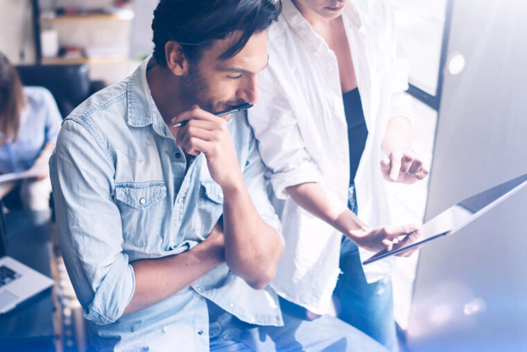 Coworking team meeting.Group of two businessmans working with new crafting startup project in sunny office.Touch pad in woman hands. Panoramic windows on blurred background.Closeup